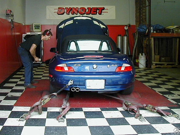 Unorthodox Pulleys-008 The car is strapped down onto the dynomometer by 4 belts. 2 lower belts go straight, and the upper 2 angle in to keep the car from moving. Alain is in the...